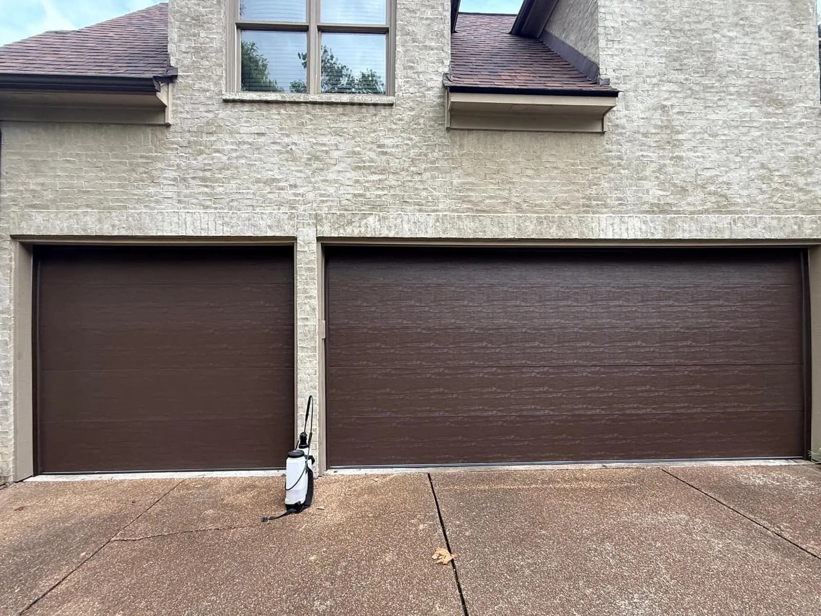 Brown flush-panel single and double garage doors on a brick home