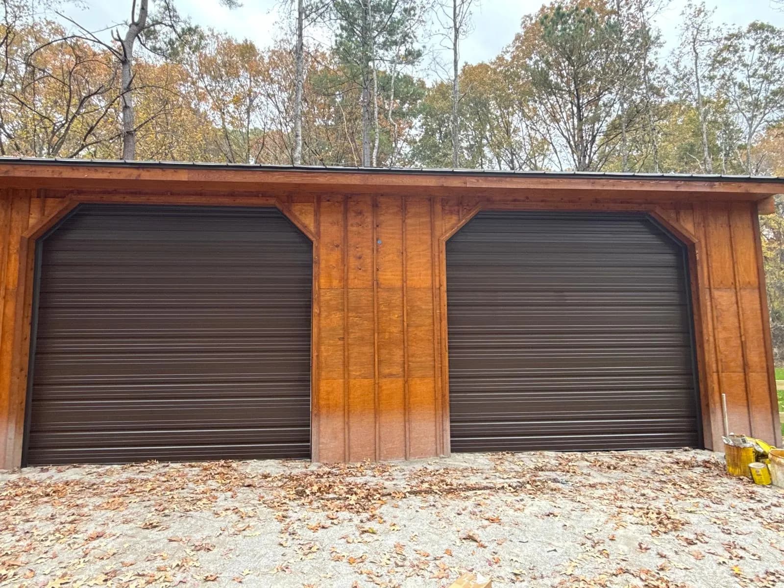 Two brown roll-up garage doors on a wood-sided building