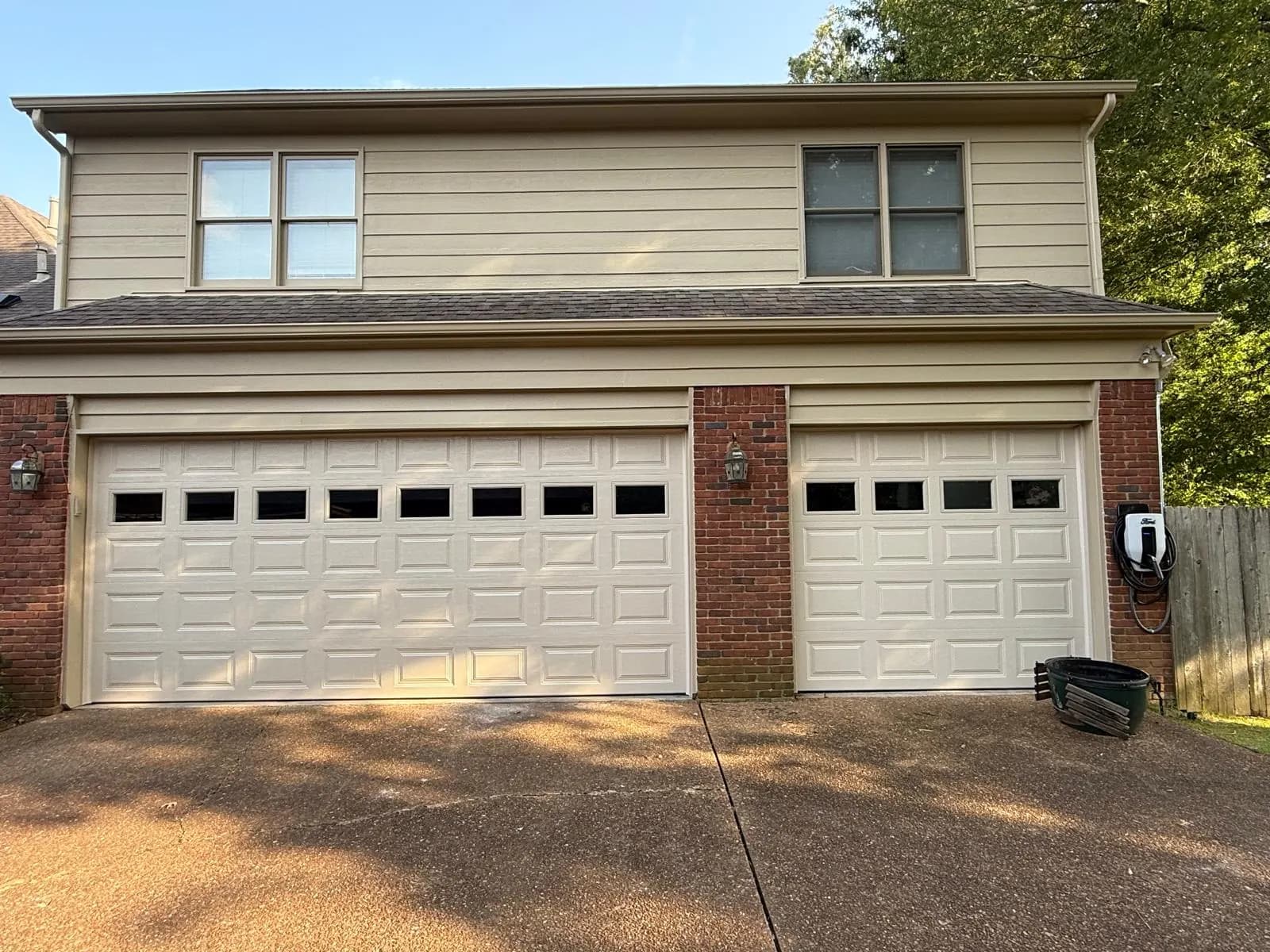 Three light-colored raised-panel garage doors with top windows